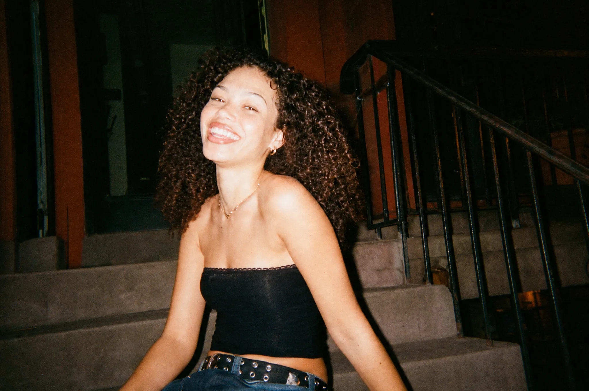 A woman laughing on a rowhouse stoop at night, lit by a disposable camera flash